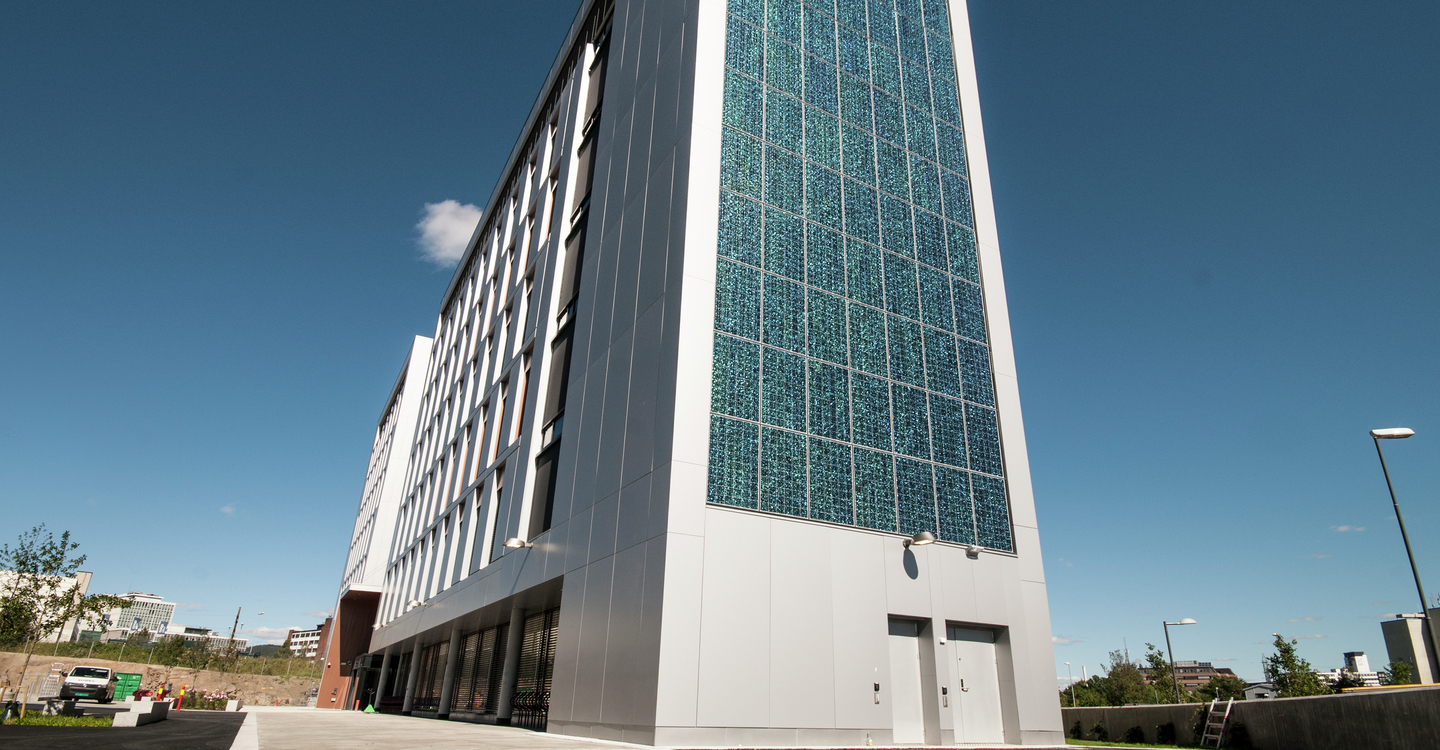 Stort hus med solcellepaneler mot blå himmel. Det er Karvesvingen 3 hvor Bymiljøetaten holder til.